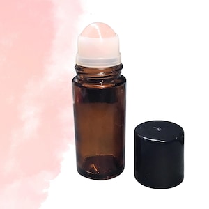May include: A small, brown glass roller bottle with a white rollerball and a black cap. The bottle is cylindrical and appears to be empty. The cap is placed next to the bottle.