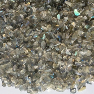 May include: A close-up of a pile of iridescent gray labradorite chips. The chips are various sizes and shapes, with a shimmering, reflective surface.