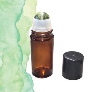 May include: A small, amber glass roller bottle with a white rollerball top and a separate black cap. The rollerball is a green and white stone. The bottle is empty and ready to be filled with essential oils or perfume.