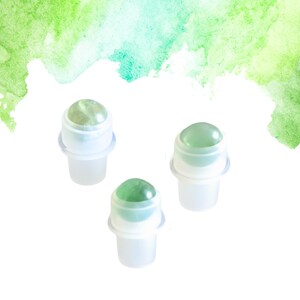 May include: Three clear glass roller bottles with green gemstone tops are set against a watercolour background of green and light blue hues. The bottles have white plastic components and are evenly spaced.