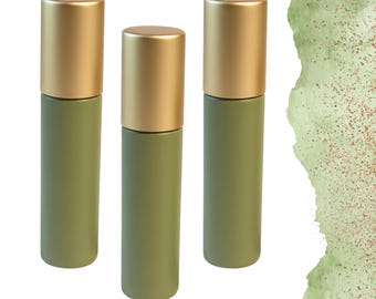 Könnte beinhalten: Drei olivgrüne Roll-on-Flaschen mit goldfarbenen Kappen. Die Flaschen sind zylindrisch und stehen aufrecht vor einem weißen Hintergrund mit einem grünen Aquarelldesign in der oberen rechten Ecke.