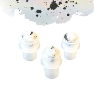 May include: Three small, white, cylindrical containers with a rounded top, each filled with a light-coloured substance speckled with dark flecks. The containers are arranged in a triangular formation against a white background.