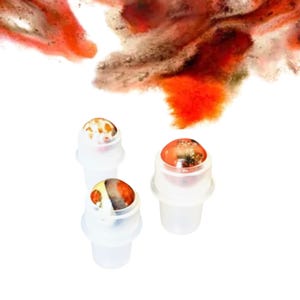 May include: Three clear plastic roller bottles with marbled tops in shades of orange, brown, and yellow. The background features an abstract design in similar colours.