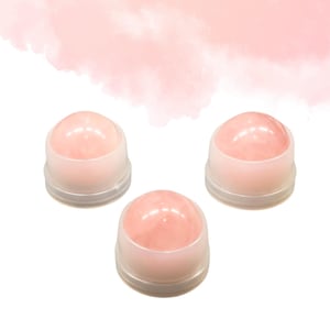 Può includere: Tre rollerball di cristallo rosa con base in plastica trasparente sono disposti su sfondo bianco. I rollerball hanno una forma liscia e arrotondata e un colore rosa tenue. Lo sfondo presenta un lavaggio ad acquerello rosa.