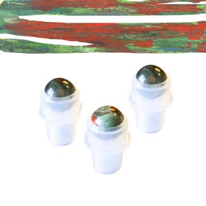 May include: Three clear, plastic roller bottles with a gemstone top. The gemstone is a mix of dark green, red, and black. The background is white with a painted abstract design of red, green, and brown.