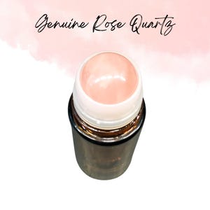 May include: A rose quartz roller with a light pink gemstone top and a metallic, cylindrical base. The text "Genuine Rose Quartz" is written in cursive above the roller. The background is a soft pink watercolor wash.