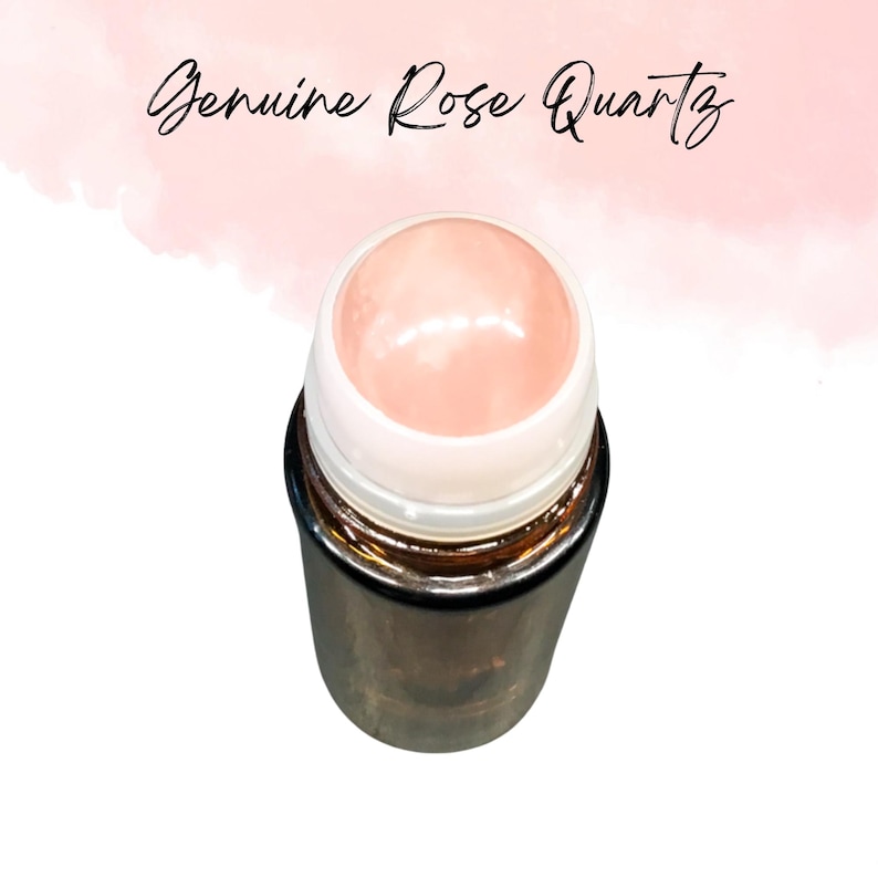May include: A rose quartz roller with a light pink gemstone top and a metallic, cylindrical base. The text "Genuine Rose Quartz" is written in cursive above the roller. The background is a soft pink watercolor wash.