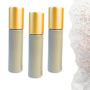 May include: Three cylindrical bottles with gold-colored caps. The bodies of the bottles are a light gray color. The background is white with a watercolor-style design on the right side.