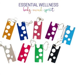 May include: Assortment of ten colorful metal keychains with three round holes each. The keychains are arranged in two rows on a white background. The text "ESSENTIAL WELLNESS body.mind.spirit" is at the top of the image.