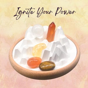 Op de afbeelding: Een houten dienblad toont een witte geometrische bergketen met diverse kristallen. De kristallen omvatten een heldere bol, een oranje kristalpunt, een gele kristal, een oranje steen en een bruin-gouden steen. De tekst "Ignite Your Power" staat erboven.