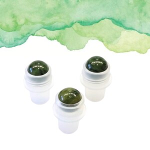 May include: Three jade roller bottles with green gemstone tops and white plastic bases. The background features a watercolour wash of green hues. These rollers are designed for skincare and beauty routines.