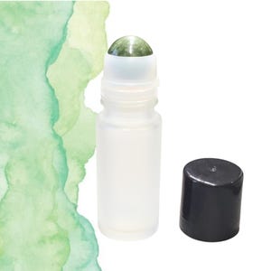 May include: A frosted glass roller bottle with a green gemstone rollerball and a separate black cap. The bottle is empty and ready to be filled with essential oils or other liquids. The background is white with green watercolor strokes.