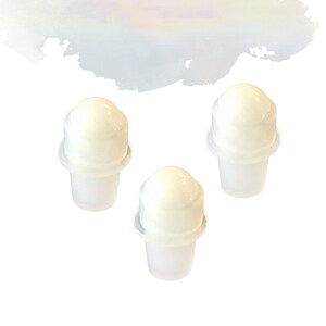 May include: Three white bottle stoppers, each with a cone-shaped base and a rounded top. The stoppers have a two-part design. The background is white with a soft, watercolour-like wash at the top.