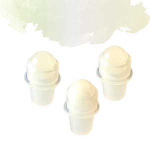 May include: Three clear roll-on deodorant applicators. Each applicator has a rounded top and a cylindrical base. The applicators are white with a light blue ring around the top of the base. The background is white with a soft green and yellow watercolour wash.