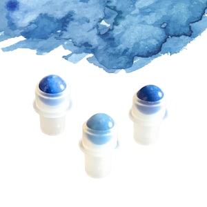 May include: Three small, white roller bottles with blue gemstone tops are shown against a watercolour blue wash background. The rollerballs vary in shades of blue, from light to dark.