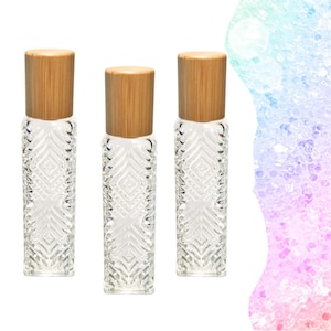 Puede incluir: Tres frascos roll-on de vidrio transparente con un patrón de diamantes texturizado y tapas de madera natural. Los frascos son cilíndricos y están diseñados para aceites esenciales o perfumes. Las tapas son de color marrón claro.
