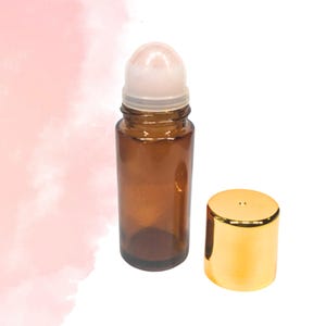 May include: A brown glass roller bottle with a white rollerball and a gold cap. The bottle is empty and ready to be filled with essential oils or perfumes. The cap is off to the side.