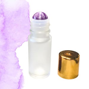 以下が含まれることがあります： 紫のアメジストローラーボールと金色のキャップが付いた、つや消しガラスのエッセンシャルオイルローラーボトル。ボトルは空で、キャップは横にあります。紫色の水彩画が背景にあります。