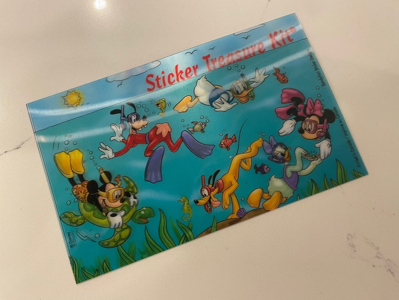 May include: A sticker treasure kit featuring Mickey Mouse, Minnie Mouse, Goofy, Pluto, and Donald Duck. The characters are all underwater and surrounded by bubbles and fish. The kit includes a variety of stickers that can be used to decorate notebooks, journals, and other items.