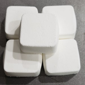 May include: Five white bath bombs stacked on top of each other. The bath bombs are square shaped and have a rough texture.