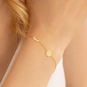 May include: A gold chain bracelet with a small paw print charm and a letter 'E' charm.