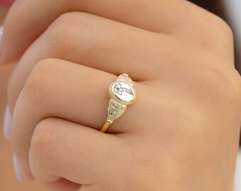 May include: A gold signet ring with an oval shaped top featuring a delicate floral design.