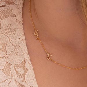 以下が含まれることがあります： ダイヤモンドがちりばめられた小さな文字が3つ付いた、金のチェーンネックレスです。