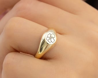 May include: A gold signet ring with a flower design engraved on the top.