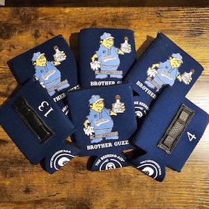 May include: Navy blue drink koozies with a cartoon graphic of a man holding a bottle, with the text "Brother Guzz" and "El Paso, Texas". Some koozies have numbers and black leather accents. The website www.beeringaid.com is also visible.