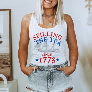 May include: White tank top with a red, white and blue graphic that says "Spilling the Tea Since 1773" and a drawing of a ship.