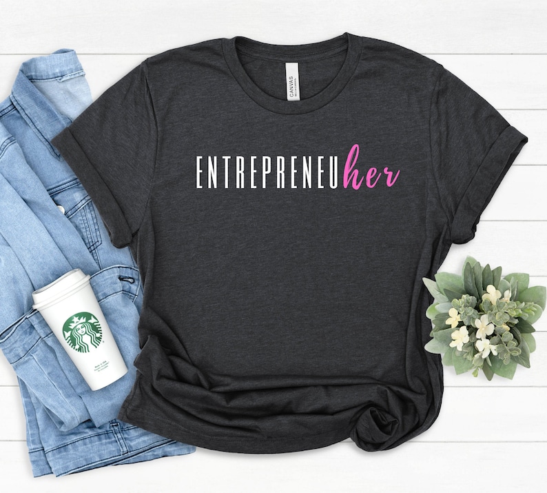 May include: A dark gray t-shirt with the text "ENTREPRENEUher" in white and pink lettering. The word "her" is in pink.