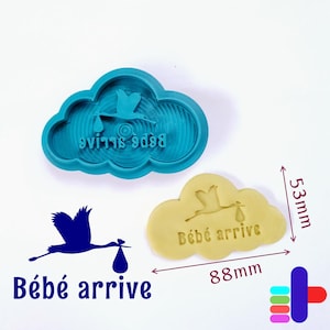May include: A teal cloud-shaped cookie cutter with a stork design and the words "Bébé arrive" in reverse. A yellow cookie with the same design is next to it. The cookie is 88mm long and 53mm high.