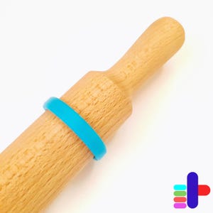 Puede incluir: Un rodillo de madera con una banda de silicona azul brillante. El rodillo es de madera clara y tiene una forma cilíndrica lisa. La banda azul añade un toque de color y está colocada alrededor del centro del rodillo.