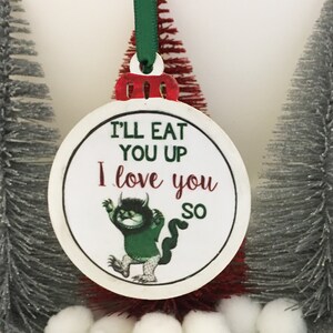 May include: A round white Christmas ornament with a green and black illustration of a monster. The ornament has the text "I'll eat you up I love you so" on it.