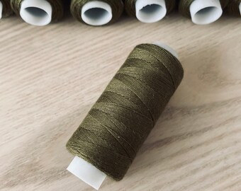 May include: A spool of olive green thread with a white plastic bobbin.
