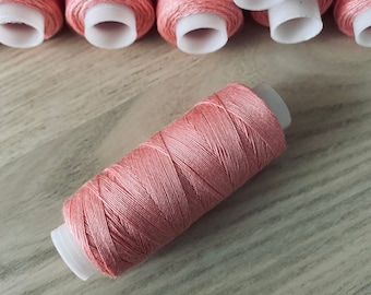 May include: A close-up of a single pink thread spool on a wooden surface. Several other spools of the same color are visible in the background.
