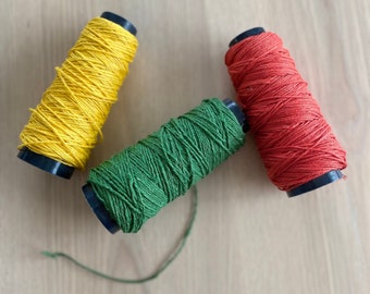 May include: Three spools of thread, one yellow, one green, and one red, are arranged on a wooden surface.