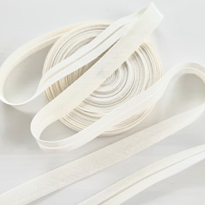 Peut inclure: Un rouleau de biais blanc cassé avec plusieurs longueurs déroulées. Le ruban est fait d'un tissu tissé. Le biais est probablement utilisé pour les projets de couture et d'artisanat.
