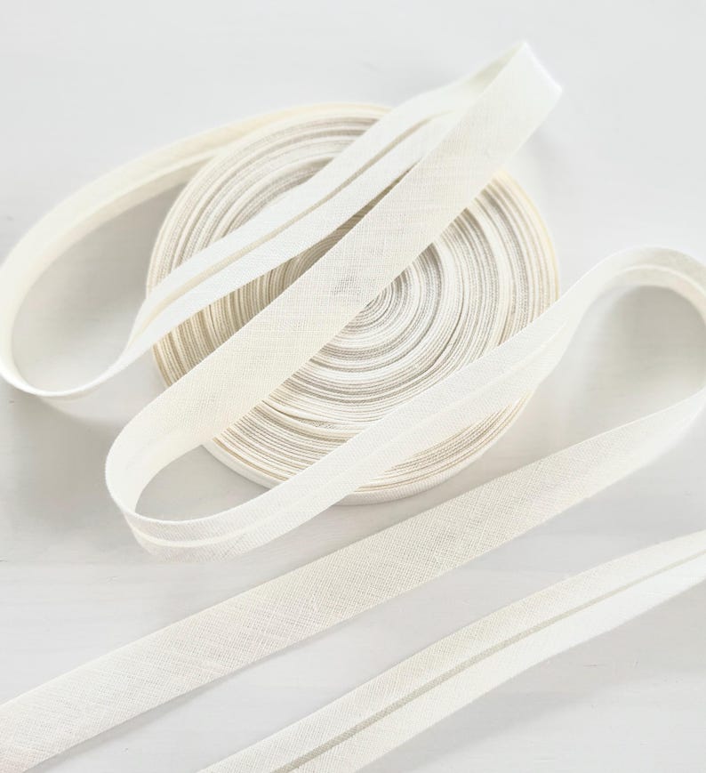 May include: A roll of cream-coloured bias binding with several lengths unrolled. The tape is made of a woven fabric. The bias binding is likely used for sewing and craft projects.