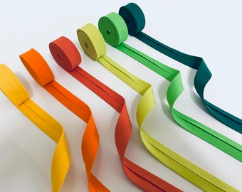 May include: Five rolls of bias tape in various colors, including orange, yellow, green, and teal. The tape is folded in half and has a seam down the center.