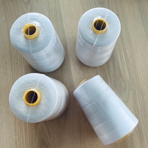 May include: Four spools of white thread with yellow plastic bobbins. The spools are on a wooden surface.