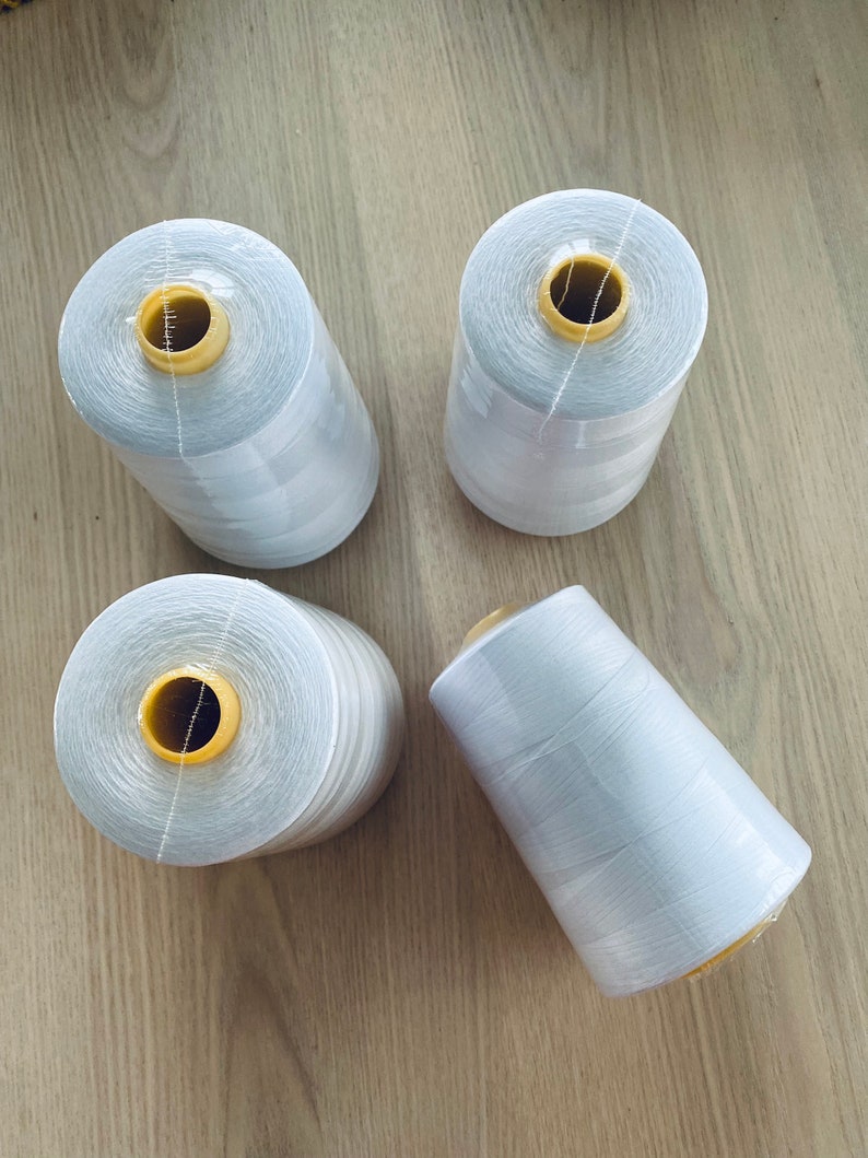 May include: Four spools of white thread with yellow plastic bobbins. The spools are on a wooden surface.