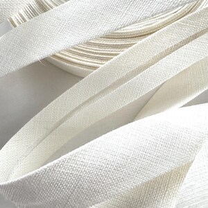 May include: Close-up of white bias binding, showing a textured weave, in a roll and several lengths. The tape is a bright, clean white, suggesting a fabric craft supply. The image highlights the texture and folds of the binding.