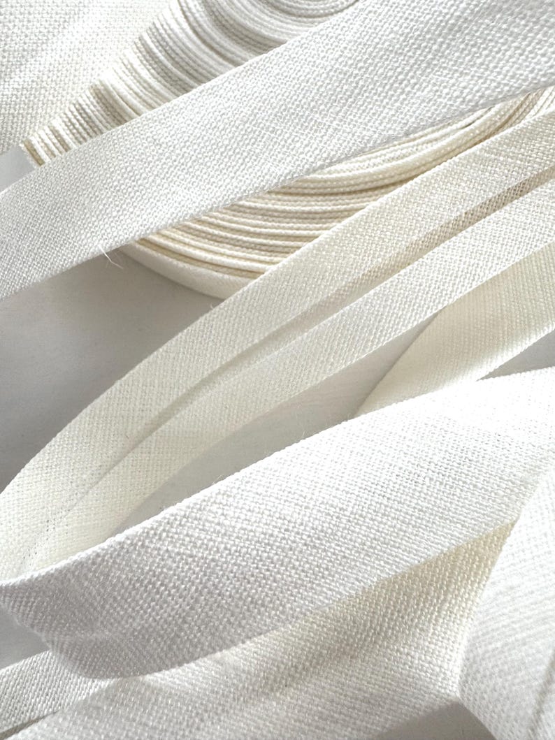 May include: Close-up of white bias binding, showing a textured weave, in a roll and several lengths. The tape is a bright, clean white, suggesting a fabric craft supply. The image highlights the texture and folds of the binding.