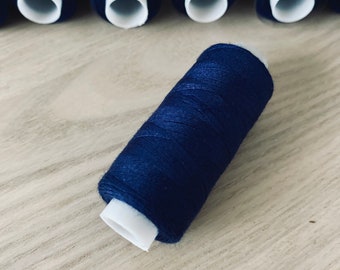 May include: A close-up of a spool of dark blue thread. The thread is wound tightly around the spool and has a white plastic centre.