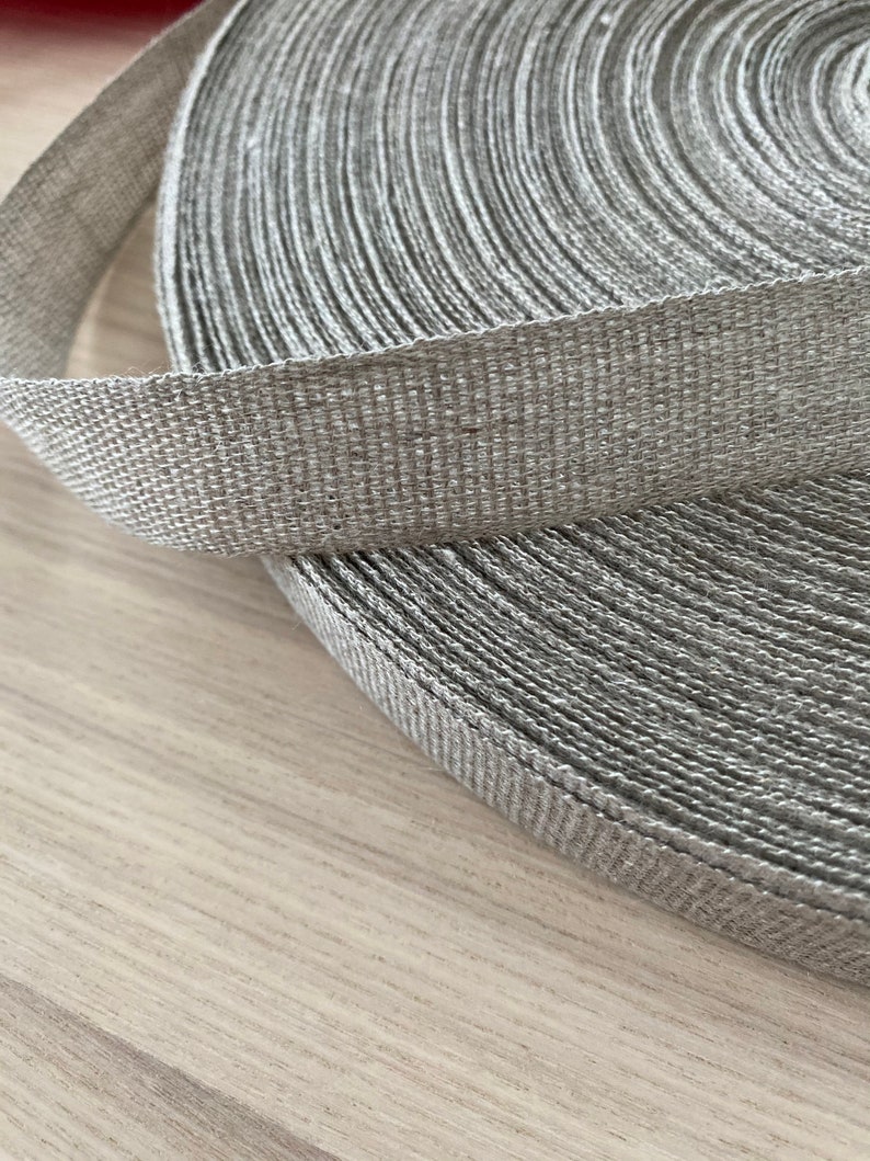 May include: A roll of gray woven ribbon. The ribbon is made of a natural fiber and has a textured surface.
