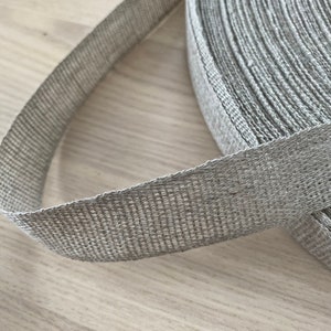 May include: A roll of gray, woven ribbon with a textured surface.