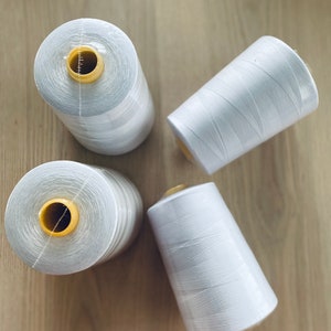 May include: Four spools of white thread with yellow plastic bobbins. The spools are arranged in a circle on a wooden surface.