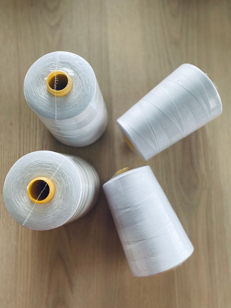 May include: Four spools of white thread with yellow plastic bobbins. The spools are arranged in a circle on a wooden surface.