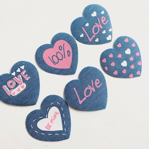May include: Six blue felt heart-shaped patches with pink and white lettering. The patches say "Love", "100%", "Love", "Be Mine", and "Love" with a pattern of small hearts.
